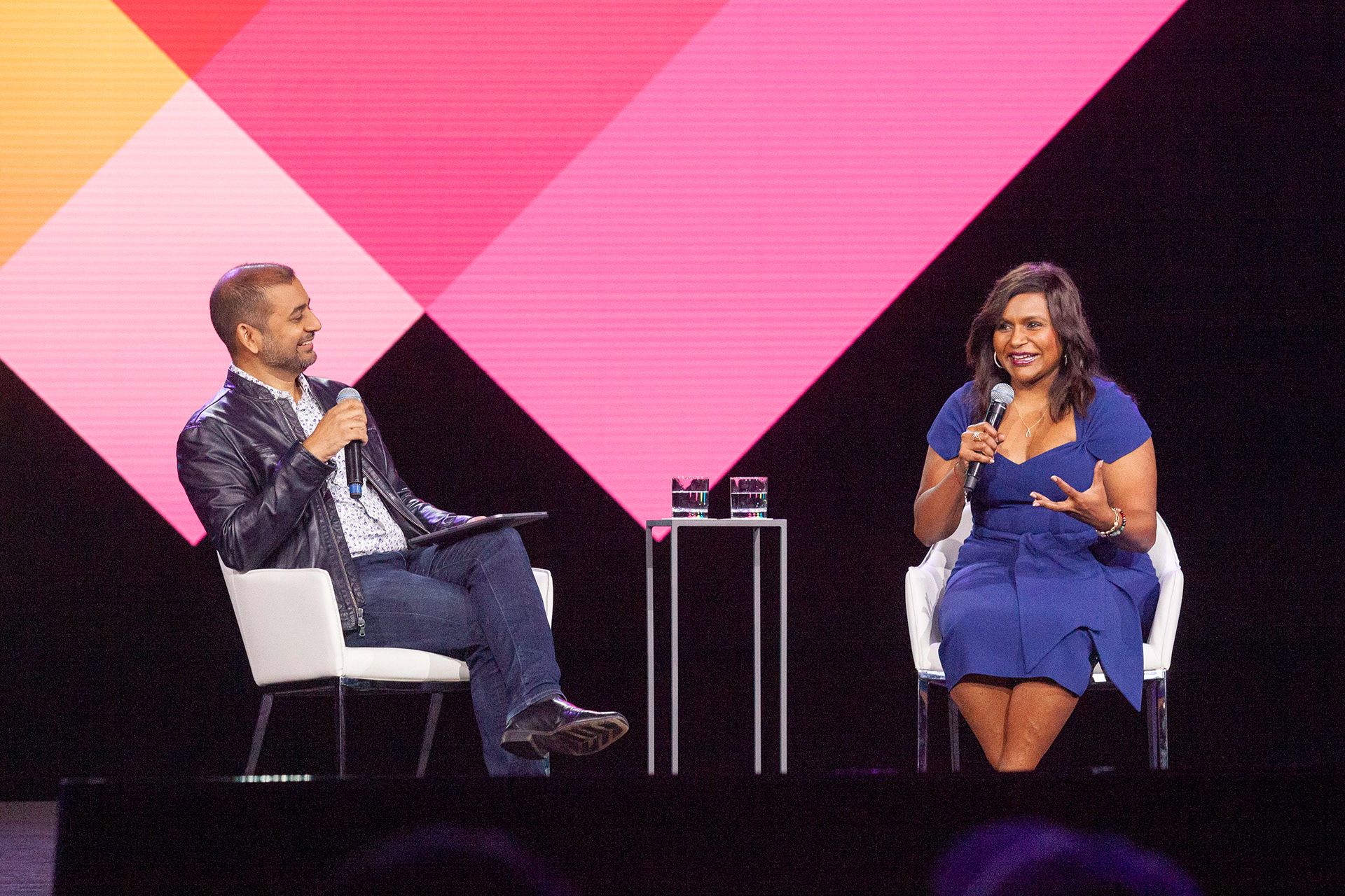 Two-person fireside chat on stage with vibrant pink geometric backdrop
